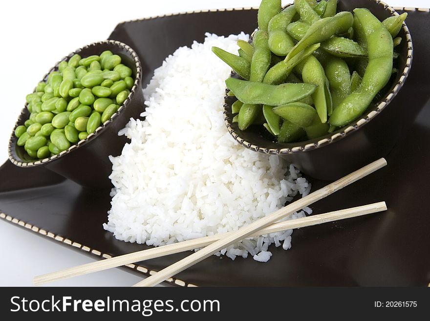 Edamame soy beans both shelled and un-shelled with chopsticks with white rice in a brown ceramic dish. Edamame soy beans both shelled and un-shelled with chopsticks with white rice in a brown ceramic dish