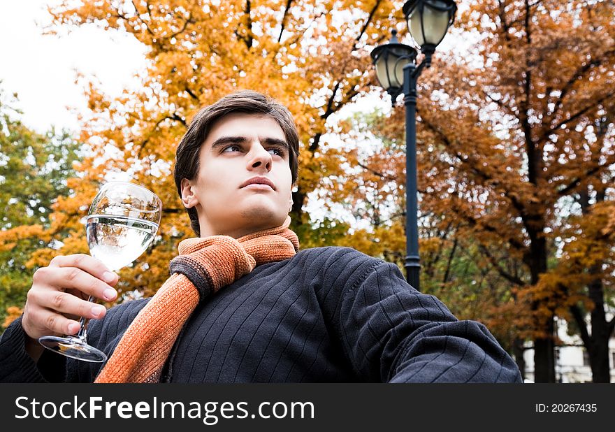 Portrait of young male holding glass of water in park on autumn day looking serious. Portrait of young male holding glass of water in park on autumn day looking serious