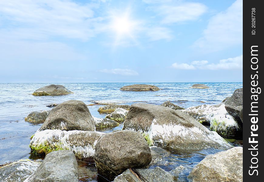 Stones into the sea on sunny sky background