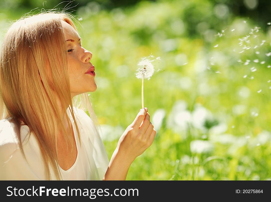 Girl blowing on a dandelion lying on the grass