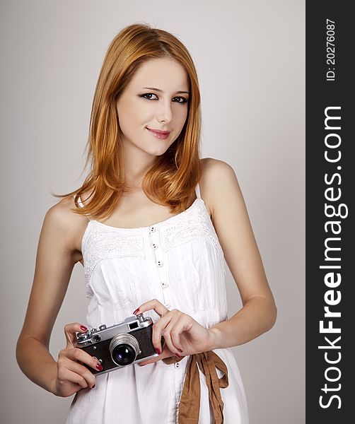 Redhead girl in white dress with vintage camera. Studio shot.