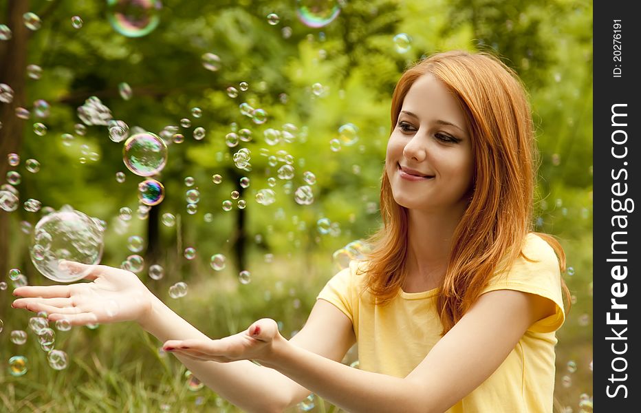 Redhead girl in the park under soap bubble rain.