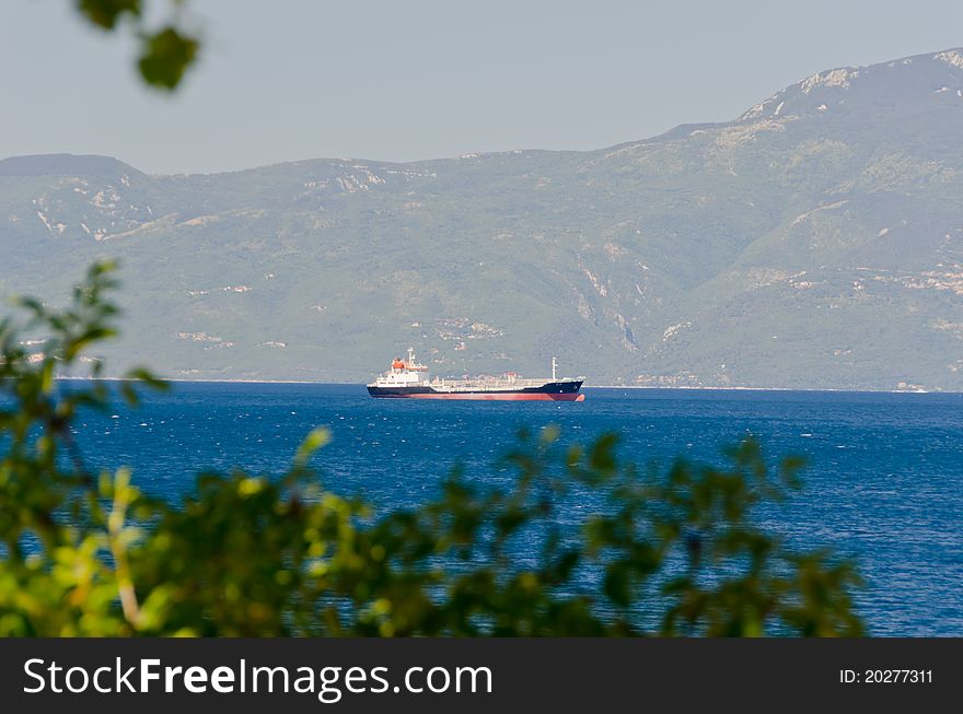 Cargo boat cruising near mountain shore, first plan are blurred plants. Cargo boat cruising near mountain shore, first plan are blurred plants