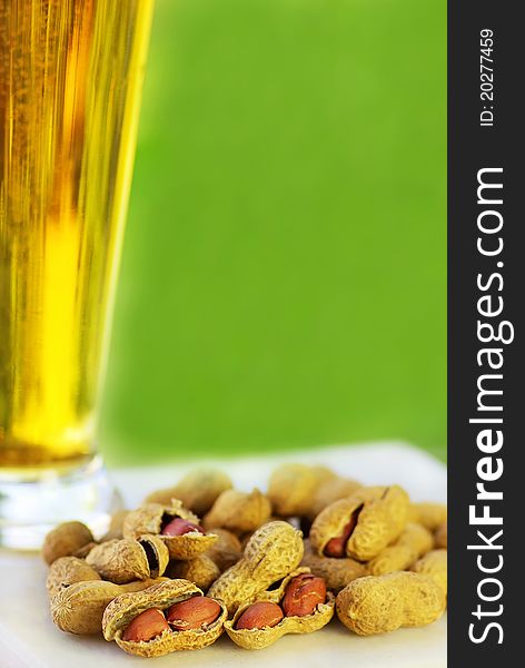 Glass of cold beer with peanuts ongreen background