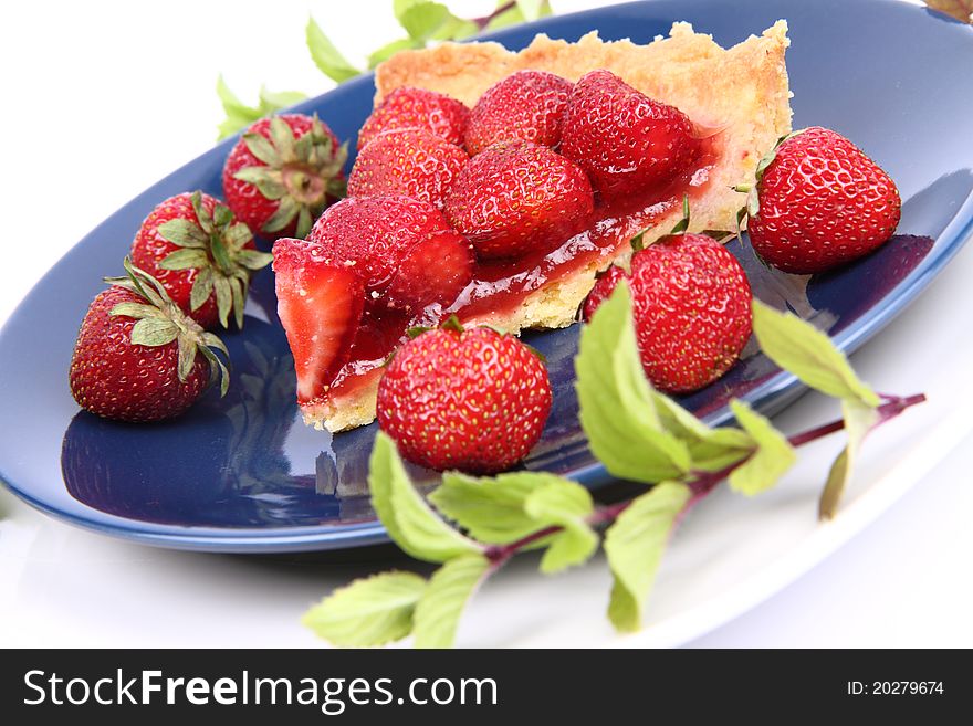 Piece of Strawberry Tart on white plate decorated with strawberries and mint twigs