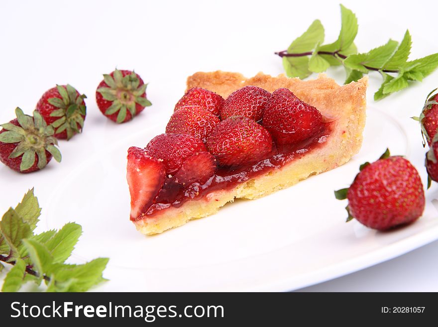 Piece of Strawberry Tart on white plate decorated with strawberries and mint twigs