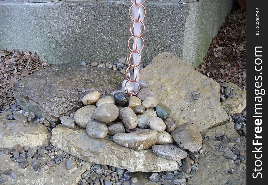 A copper rain chain in action running over river rocks