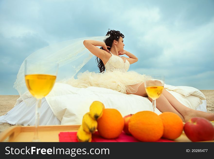 Young bride in bed at the coastline against cloudy sky