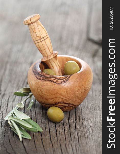 Green olives in the bowl and olive branch on wooden table