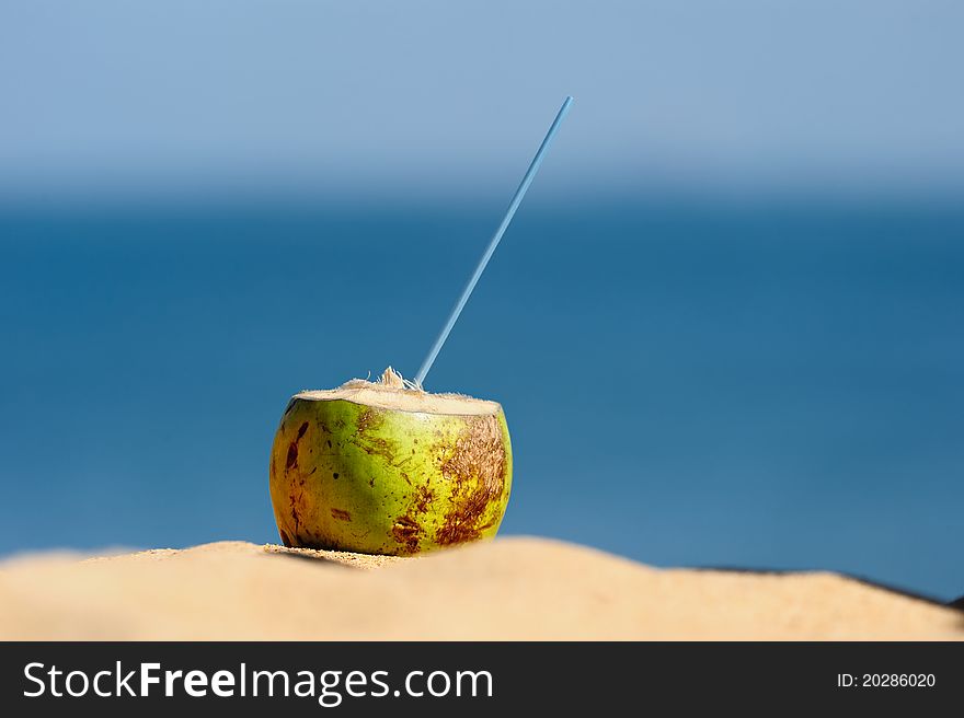 Coconut with drinking straw on the sand at the sea. Coconut with drinking straw on the sand at the sea