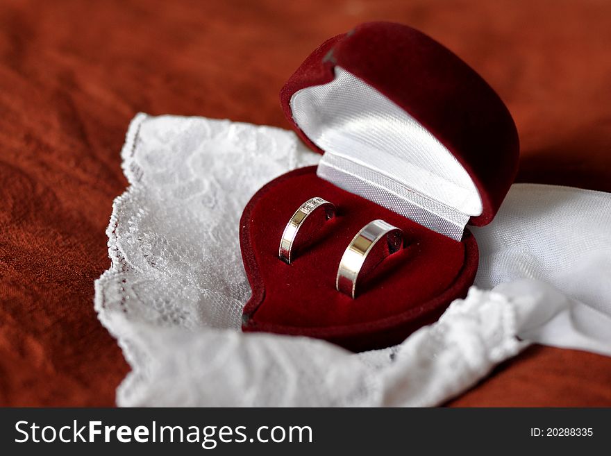 Red heart shaped box with two white-golden wedding rings