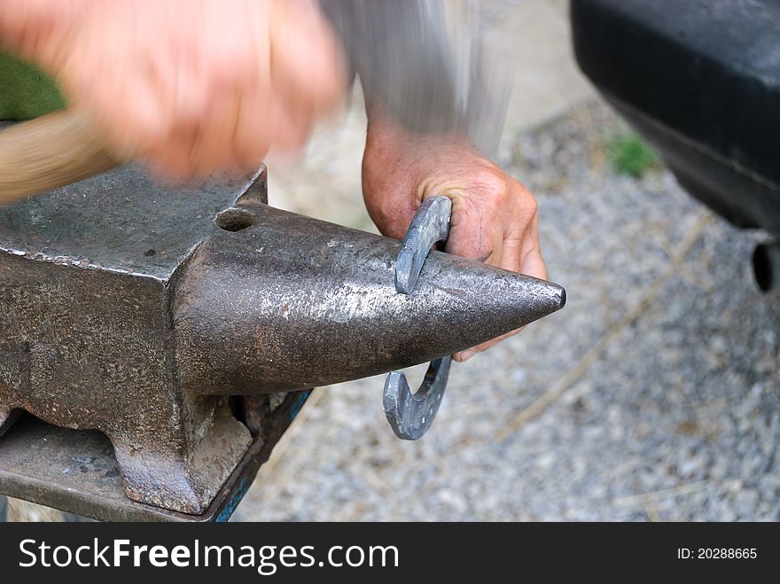 Blacksmith while hammering a horseshoe on the anvil. Blacksmith while hammering a horseshoe on the anvil