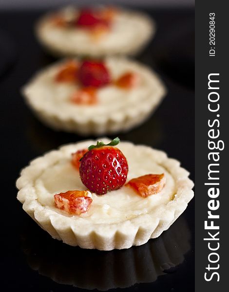 Vanilla cream and strawberry tartlets, isolated on black background