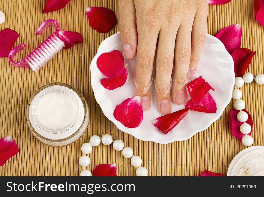 Close-up of girl's hand dropped into a saucer of water near a lot of rose petals. Spa services. Close-up of girl's hand dropped into a saucer of water near a lot of rose petals. Spa services