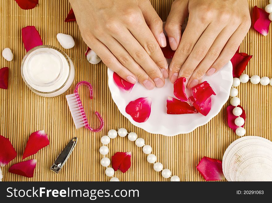 Close-up of girl's hand dropped into a saucer of water near a lot of rose petals. Spa services. Close-up of girl's hand dropped into a saucer of water near a lot of rose petals. Spa services