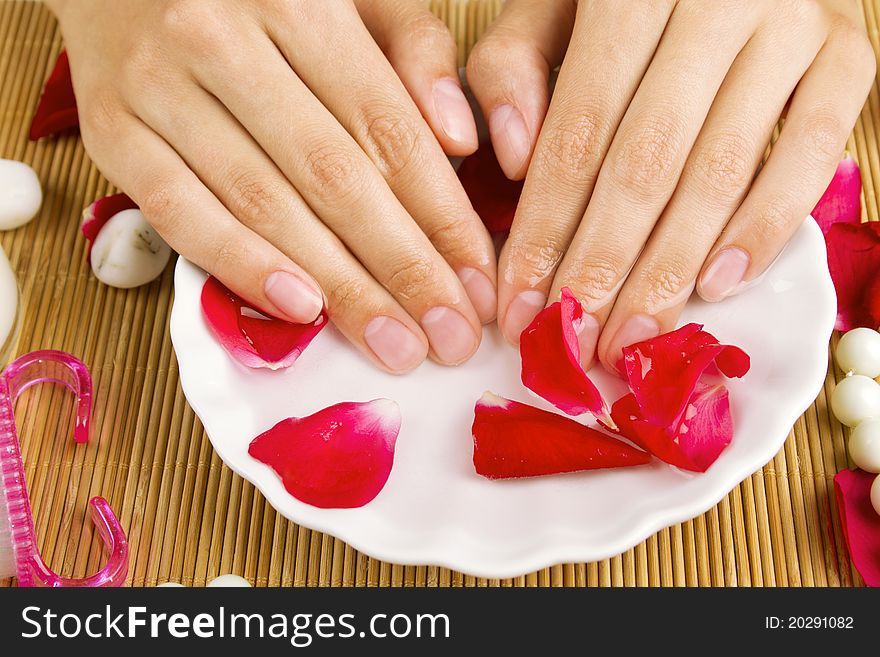 Close-up of girl's hand dropped into a saucer of water near a lot of rose petals. Spa services. Close-up of girl's hand dropped into a saucer of water near a lot of rose petals. Spa services