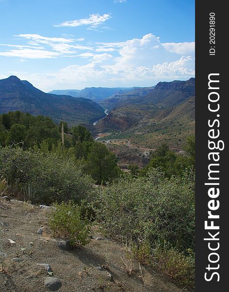 A beautiful desert canyon with a river running through it and a blue sky with white clouds and green plants. A beautiful desert canyon with a river running through it and a blue sky with white clouds and green plants