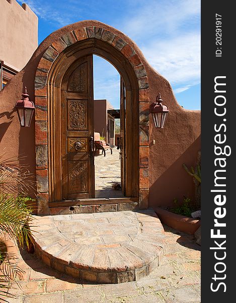 Large, arched, ornate, double door, with brick patio leading to an inner courtyard with seating. Large, arched, ornate, double door, with brick patio leading to an inner courtyard with seating