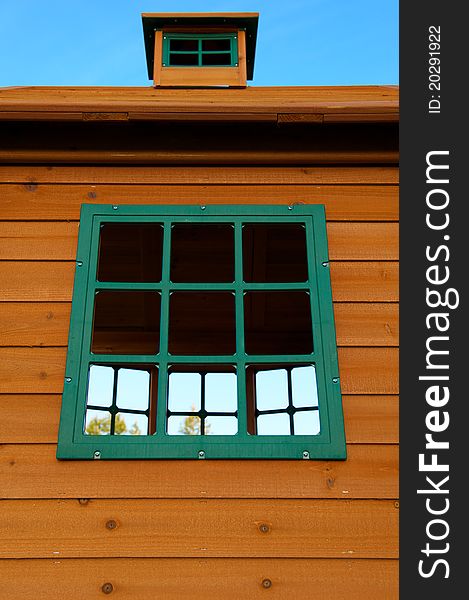 A Wooden House with knots and Green Plastic Windows that look out to trees and a blue sky. A Wooden House with knots and Green Plastic Windows that look out to trees and a blue sky