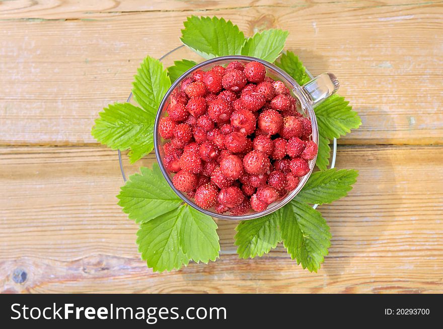 Strawberries. Wild strawberry. Strawberries in a glass bowl on a wooden table. The strawberries and green leaves.