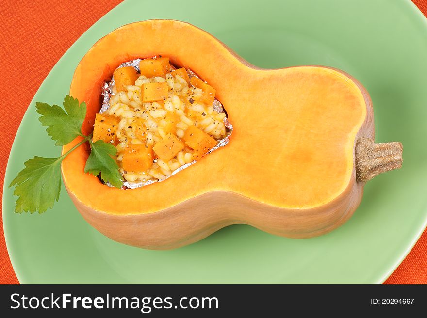 Half pumpkin filled with pumpkin risotto served on a green plate