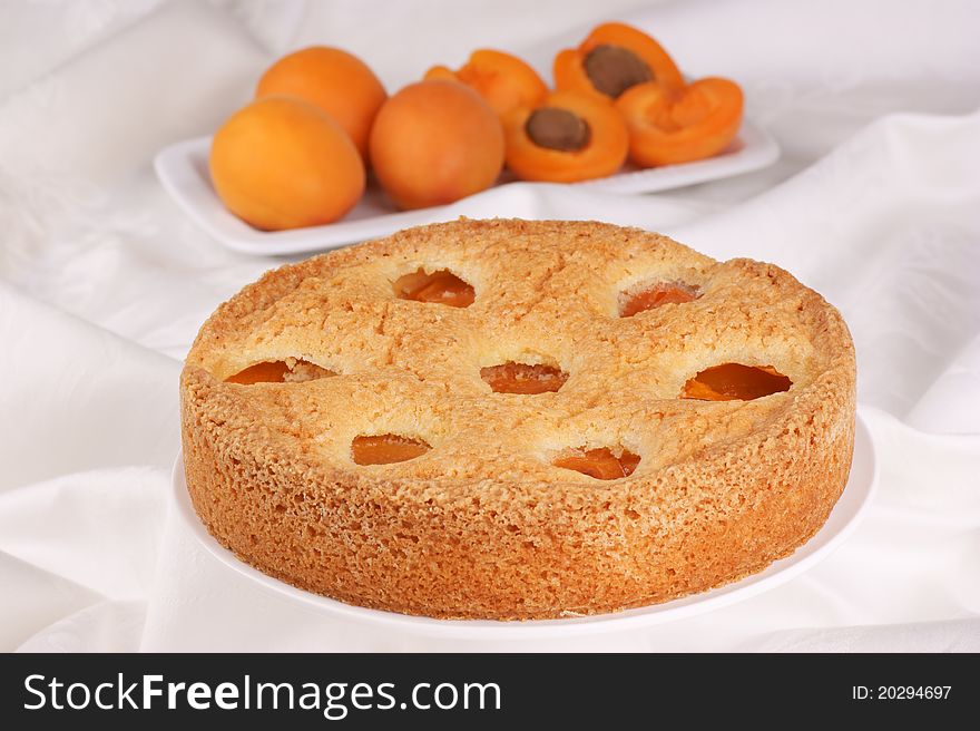 Apricot cake on a awhite cake stand. Apricots out of focus in the background