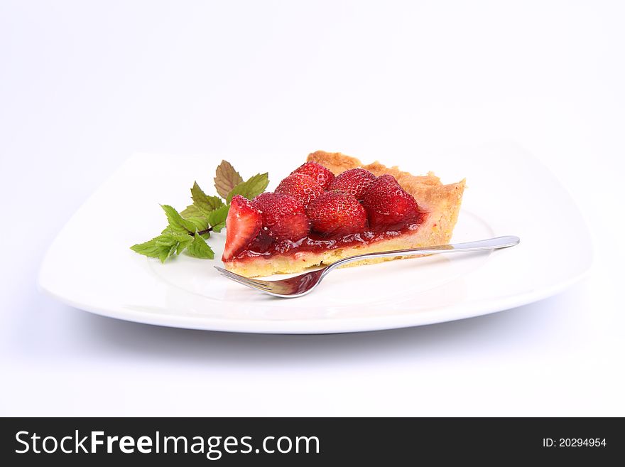 Piece of Strawberry Tart on white plate decorated with mint twig