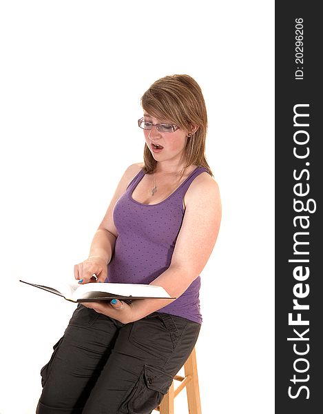 An pretty teenage girl is very surprised what she is reading in the book she is holding in her hands, sitting on a chair, over white. An pretty teenage girl is very surprised what she is reading in the book she is holding in her hands, sitting on a chair, over white.