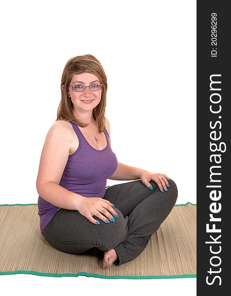 A young pretty teenager sitting on a yoga matt on the floor, with her legs grossed, smiling into the camera for white background. A young pretty teenager sitting on a yoga matt on the floor, with her legs grossed, smiling into the camera for white background.