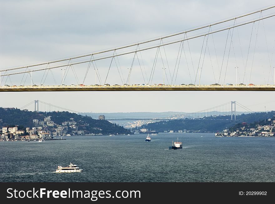 The Bosporus Bridge whcih spans the Bosphorous. Industrial Ship passing through straits of Bosphorus. Bosporus Bridge behind, Rumeli Fortress, Fatih Sultan Mehmet Bridge . Partial cloud and local sun light. The Bosporus Bridge whcih spans the Bosphorous. Industrial Ship passing through straits of Bosphorus. Bosporus Bridge behind, Rumeli Fortress, Fatih Sultan Mehmet Bridge . Partial cloud and local sun light