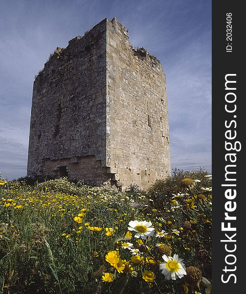 Ruined roman tower (Andalucia) from a low angle with yellow meadow flowers in the foreground. Ruined roman tower (Andalucia) from a low angle with yellow meadow flowers in the foreground