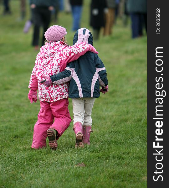 Two little girls dressed for cold weather walk away with their arms around each other. Two little girls dressed for cold weather walk away with their arms around each other