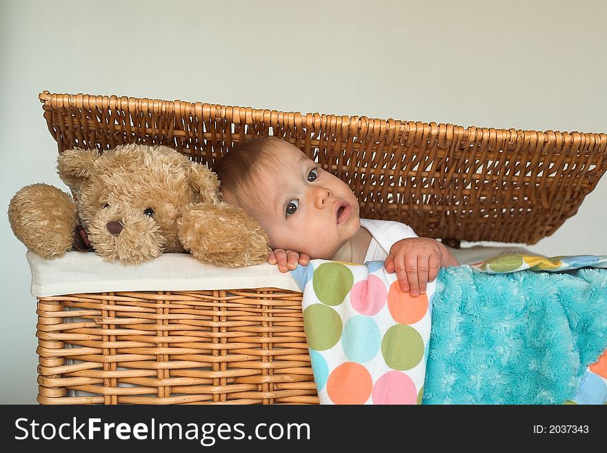 Image of cute baby and teddy bear peeking out of a wicker trunk
