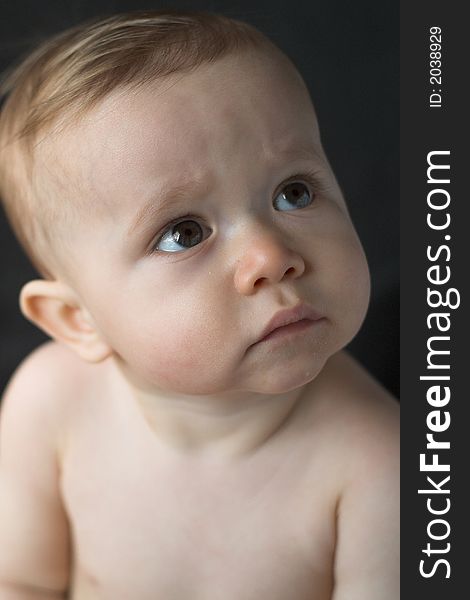 Image of a beautiful 10 month old baby boy sitting in front of a black background. Image of a beautiful 10 month old baby boy sitting in front of a black background