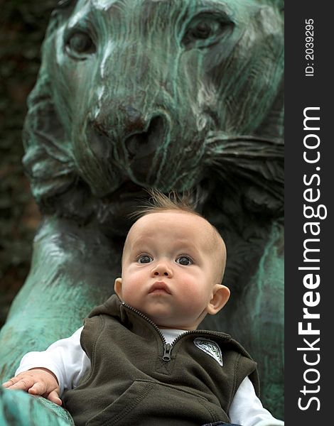 Image of cute baby sitting in front of a lion sculpture. Image of cute baby sitting in front of a lion sculpture