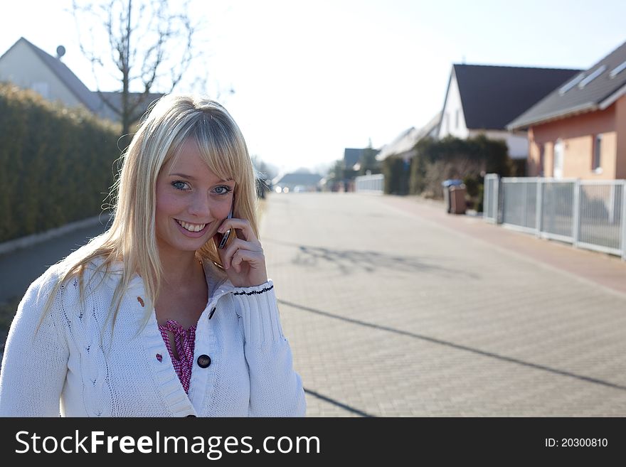 Young blond woman stands with a cell phone on a village street. Young blond woman stands with a cell phone on a village street