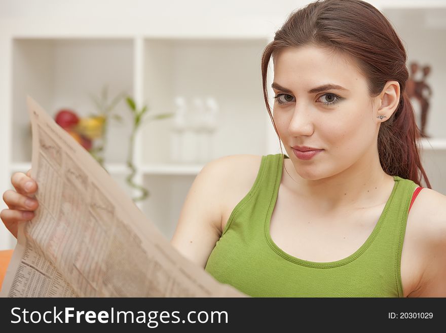 Young woman holding newspaper sitting on sofa. Young woman holding newspaper sitting on sofa