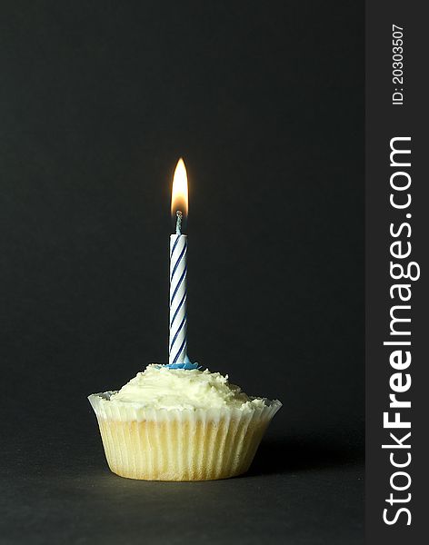 Iced cupcake with single blue birthday candle on black background. Iced cupcake with single blue birthday candle on black background