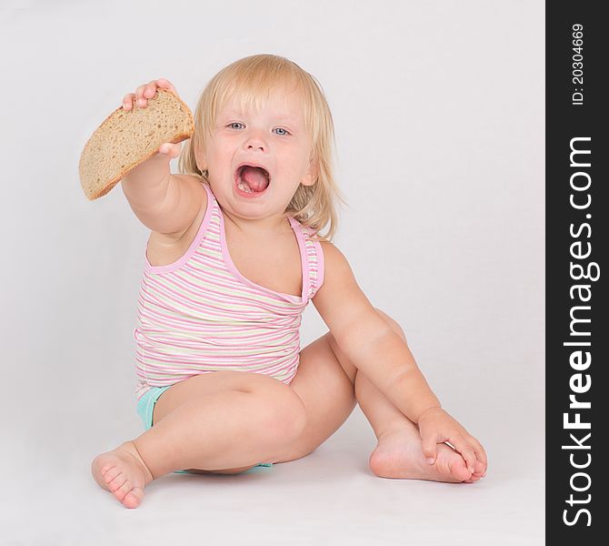 Adorable toddler girl eat rye bread sitting on white. Adorable toddler girl eat rye bread sitting on white