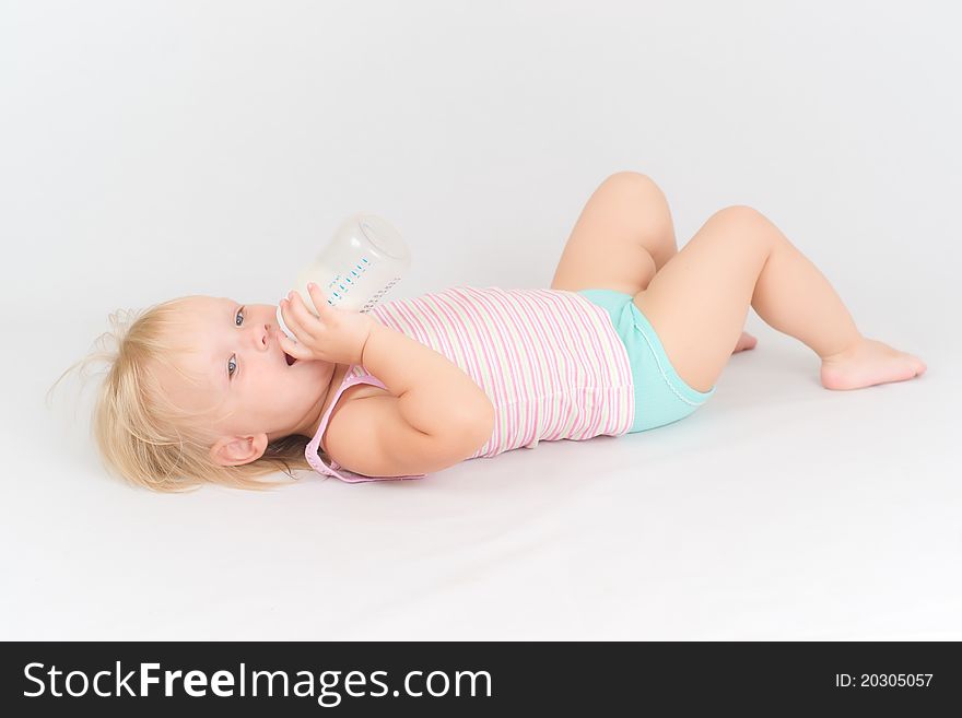 Adorable baby eating milk from the bottle lie on white floor. Adorable baby eating milk from the bottle lie on white floor