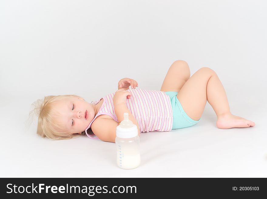 Adorable baby lie on white floor, rest after eating milk from the bottle