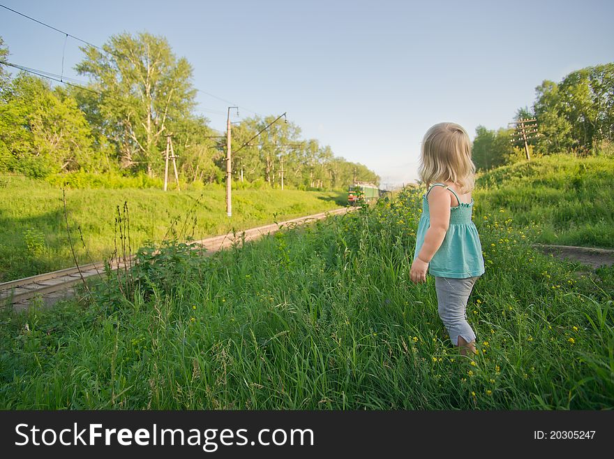 Adorable toddler girl stay on hill and look to ongoing train. Adorable toddler girl stay on hill and look to ongoing train