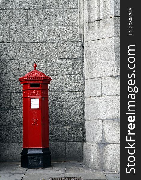 An old red free standing post box,with stone wall behind.