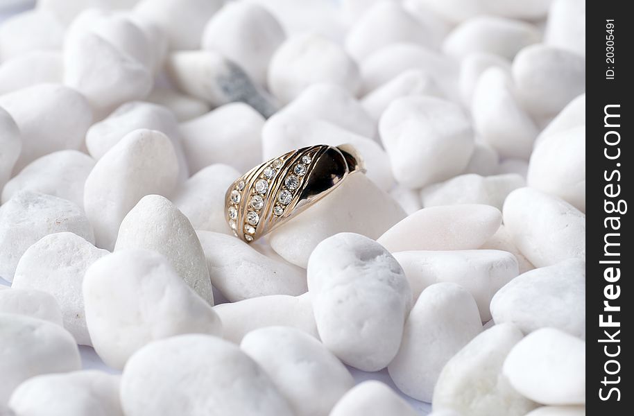 A golden ring with small crystalls on white pebble stones. A golden ring with small crystalls on white pebble stones