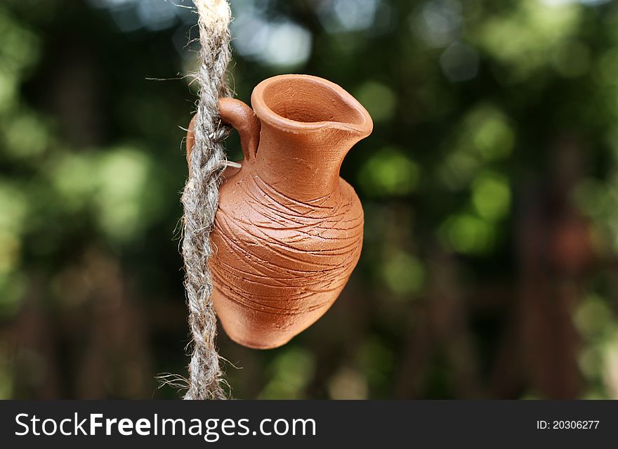 An earthen pot hanging on a rope on a background of green leaves. An earthen pot hanging on a rope on a background of green leaves