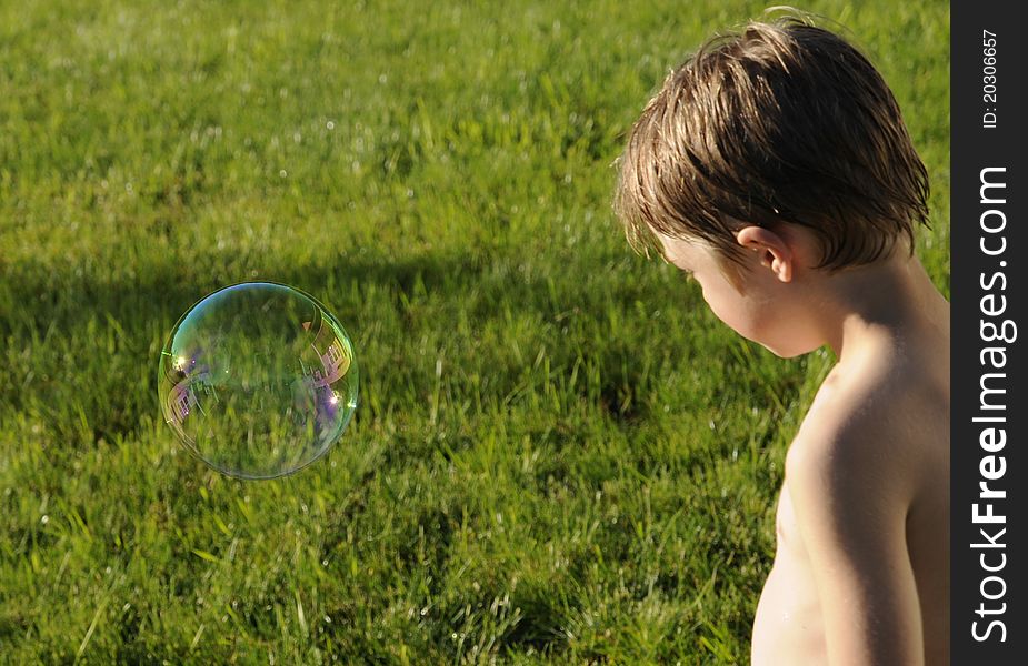 Young male looking at a freshly made bubble against a grass background. Young male looking at a freshly made bubble against a grass background