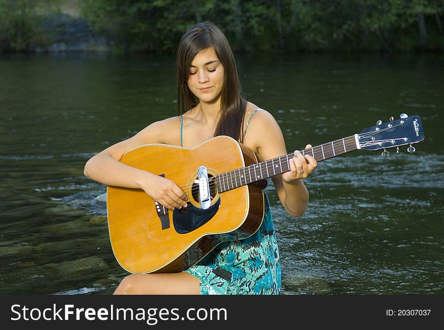 Young woman playing guitar by river in summer