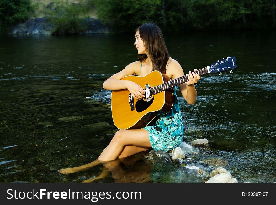 Young woman playing guitar by river in summer