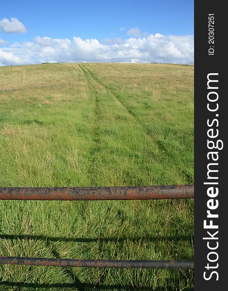 Gate and track across the fields under a blue sky, with interesting dramatic clouds. Taken in the Warwickshire countryside, England