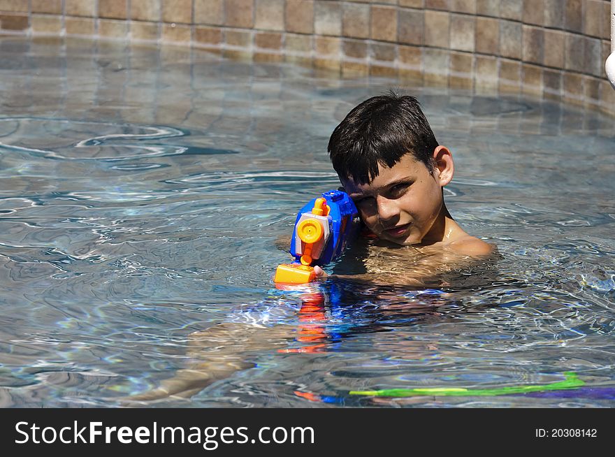 A 9 year old boy playing in the pool with a water gun. A 9 year old boy playing in the pool with a water gun.